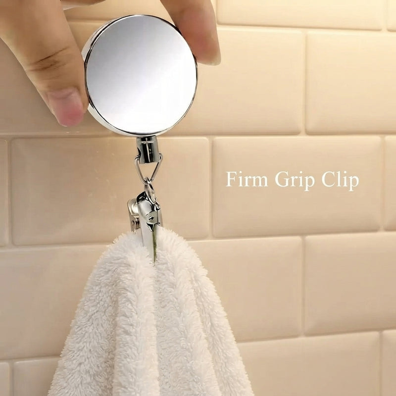 Stainless steel self-retracting towel holder clip mounted on a bathroom wall holding a white hand towel